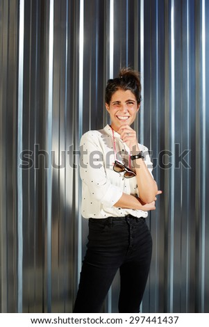 Portrait of cheerful young woman dressed in a glamorous modern clothes standing on shiny chrome background with copy space for your text message, happy teenager smiling brightly to camera in sunny day