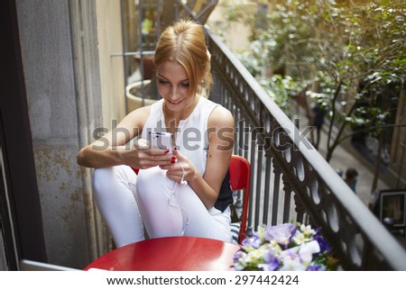 Gorgeous female enjoying recreation time while chatting with her mobile phone on terrace, smiling successful young woman read good news on the smart phone, student hold telephone looking at the screen