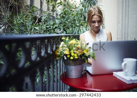 Female freelancer sitting front open laptop computer and listening to music with headphones while enjoying her breakfast,young gorgeous woman relaxing on the terrace balcony looking at net-book screen