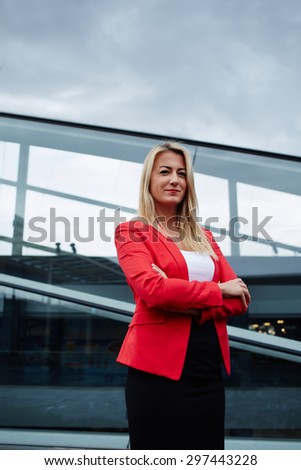 Successful businesswoman in suit standing against office building, rich luxury women in elegant clothing posing for the camera outdoors, confident female entrepreneur looking satisfied with profession