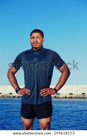 Tired male jogger taking break after an active run standing against the sky and the sea background with copy space area for your text message or advertising, muscular sportsman resting after training
