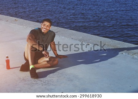 Happy sportsman taking break after workout and enjoying outdoors while sitting on the road background with copy space area for your text message or information, satisfied male jogger resting near sea