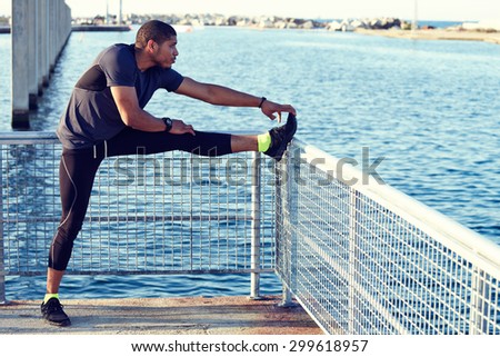 Male jogger doing stretching exercise foreleg or feet muscles above pier fence with copy space area for your text message or information content, muscular build runner preparing for workout outdoors