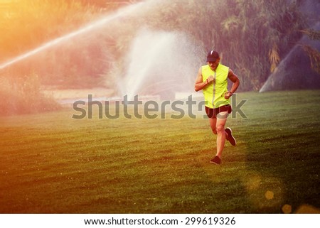 Young male runner jogging over green grass in the park with copy space area for your text message or content, healthy athlete performs physical exercises outdoors at summer afternoon, filtered image
