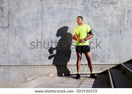 Muscular male jogger took break after workout refreshing with energy drink while standing against cement wall background with copy space area for your text message or advertising,runner having a rest