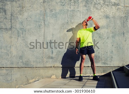 Full length portrait of sweaty man runner refreshing with energy drink water after jogging against cement wall background with copy space area for your text message or content,sportsman having a rest