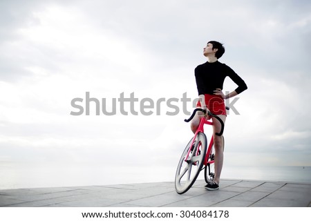 Full length portrait of stylish young woman dressed in flamboyant active wear standing with her modern sports fixed gear bicycle against copy space area cloudy sky,female hipster enjoying calm scenery