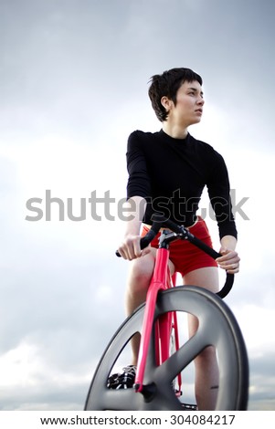 Full length portrait of professional female rider with her sport fixed gear bicycle standing on concrete pier seashore with copy space cloudy sky, woman enjoy active weekend while she riding on bike