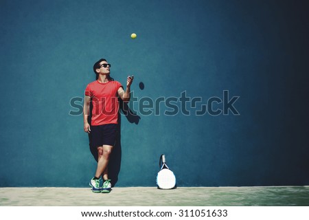Full length portrait of handsome sportsman tossing a tennis ball while taking break after paddle game in sunny day outdoors, paddle player with copy space area for text message or advertising content