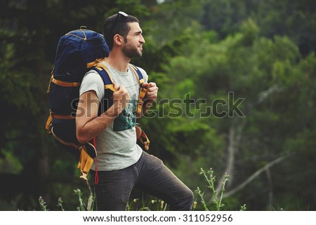 Portrait of young male backpacker with a rucksack standing on the mountain hill while enjoying nature scenery view with plants copy space area background for your text message or advertising content