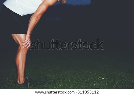 Cropped image of exhausted male jogger with muscular body taking break after run in the park while resting with hands on his knees against copy space area for your text message or advertising content