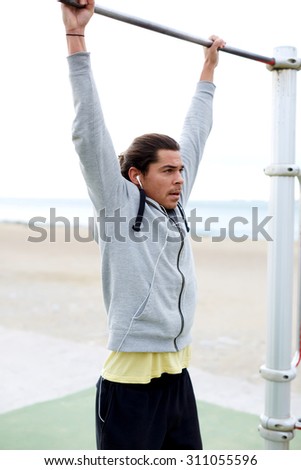 Portrait of a young handsome sportsman doing pulls ups on the horizontal bar street gym, male athlete performs exercises for the muscles near the sea, fit man engaged in physical activity outdoors