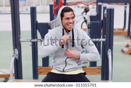 Portrait of a happy smiling sportsman having a break after workout outdoors, jogger man listening to music in headphones enjoying rest,young sporty guy resting after training sitting on sports ground