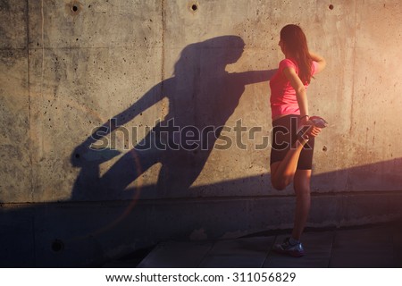 Female runner with beautiful figure doing stretching exercise before began her run, athletic woman warming up outdoors against concrete wall with copy space area for your text message or content