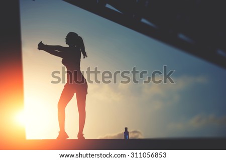 Half length portrait of sporty woman doing workout on sunset sky background in urban setting, silhouette of athletic female jogger against the sunset sky doing workout