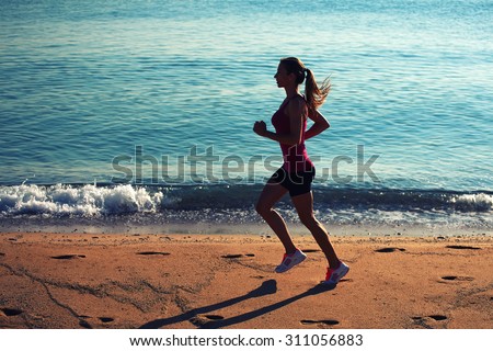 Full length portrait of purposeful woman runner with beautiful figure doing daily evening run on the beach,young female athlete with hair tied up in a ponytail engaged in active sports against the sea