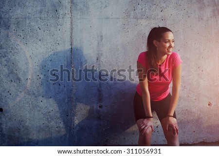 Young smiling female resting after an active fitness training while standing against gray wall with copy space area for your text message, satisfied fit woman resting after an active fitness training