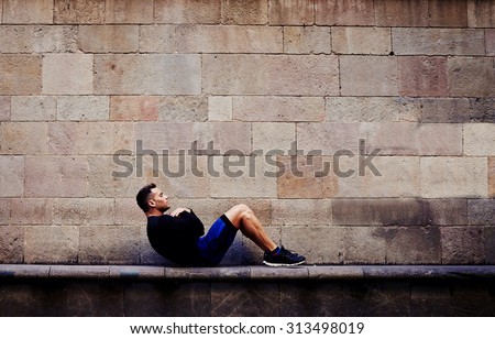 Young sportsman doing abdominal crunches against brick wall with copy space area for your text message or advertising content, sporty guy engaged an intensive fitness training in urban setting