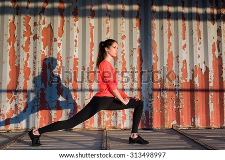 Female runner stretching her legs before began morning run at sunny morning outdoors,sports woman exercising against old metallic wall with copy space area for your text message or advertising content