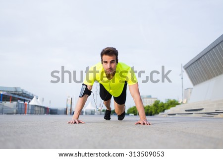 Handsome sports man doing warm up exercise before start his workout training outside, caucasian male jogger working out with hands leaning on asphalt city road while listening to music in headphones