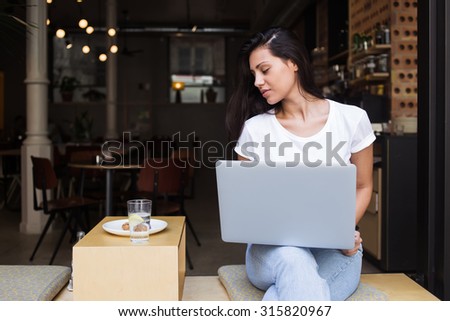 Portrait of young pretty woman using net-book for remote work while sitting in cafe outdoors, beautiful female learning via portable gadget device while sitting in modern coffee shop during breakfast