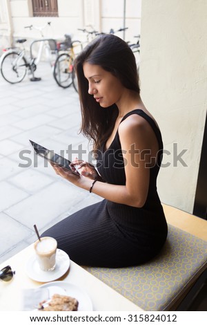 Portrait of a young charming latin women connecting to wireless on her digital tablet while sitting in cafe outdoors, university student girl working on her touch pad during coffee break in restaurant