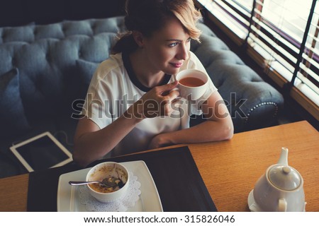 Portrait of young gorgeous female drinking tea and looking with smile out of the coffee shop window while enjoying her leisure time, nice business woman lunch in modern cafe during her work break
