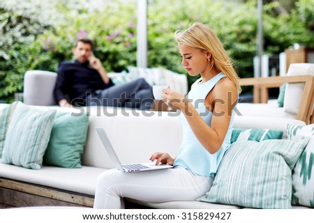 Intelligent woman entrepreneur holding cup of coffee and work on computer, female professional using laptop during her coffee break, freelancer girl work on her laptop while sitting at modern cafe