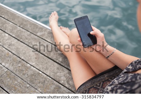 Cropped image of woman holding mobile phone with copy space area for your text message or advertising content, hipster girl chatting on her cell telephone while relaxing in the fresh air outside