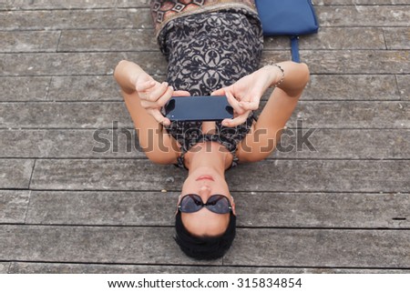 Half length portrait of brunette woman making self portrait with her smart phone digital camera while lying on a wooden flooring, female posing while photographing herself for social network picture