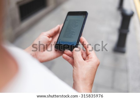 Cropped shot view of woman reading some text on her cell telephone while walking on the street, female typing text message on smart phone, screen with copy space area for your advertising content