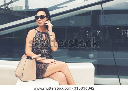 Portrait of elegant lady talk on mobile phone while relaxing after walking on the street in summer day, confidence female business woman calling with smart phone while sitting outdoors in summer day