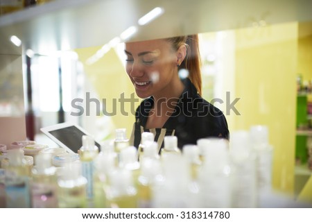 Smiling woman entrepreneur examines hygiene beauty products in her cosmetic shop, attractive female consultant or seller studying cosmetics while using digital tablet to improve service quality