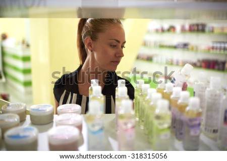 Young attractive woman consultant lays out beauty on store shelves, attractive female reads the contents of the product before making a purchase in cosmetic shops, buyer consider aromatic fluids
