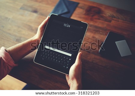 Hipster man hands holding digital tablet with empty blank screen for your text message, business person browsing internet or connecting to wireless via touchscreen pad sitting at brown wooden table