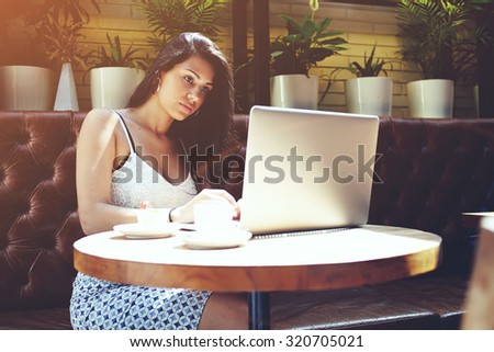 Hispanic appearance businesswoman working on laptop computer while sitting in a modern restaurant,young clever student girl sitting with open net-book and writes a text message on the keyboard
