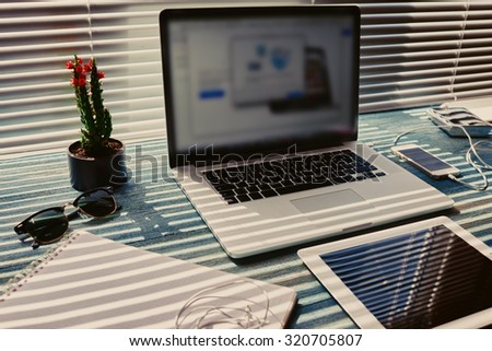Freelance desktop with accessories and distance work tools, blank screen laptop computer and digital tablet, mouse, sunglasses, phone charging and touch pad, business workspace in home or office