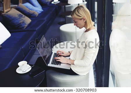 Female student connecting to wireless via laptop computer while sitting in modern coffee shop or university library, modern business woman keyboarding on net-book while working in loft studio interior