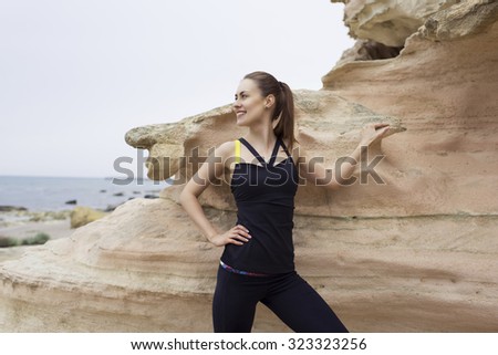 Portrait of young active woman smiles while taking break after workout outdoors in beautiful nature,female runner resting after jogging in sea and mountain rocks landscape, sportive women taking break