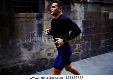 Portrait of a strong fit men dressed in sportswear jogging on the street in summer day, young athletic male running outdoors, handsome sportsmen engaged in physical exercise in the fresh air