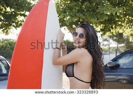Portrait of a young smiling Latin women with long luxury hair holding surfboard while standing outdoors in sunny day, gorgeous female posing before her surfing on the sea during summer weekend
