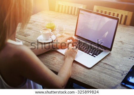 Cropped shot view of young woman keyboarding on laptop computer with blank copy space screen while sitting in cafe, blonde female student working on net-book after her lectures in University,flare sun