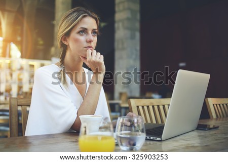 Successful charming businesswomen sitting with net-book in cozy restaurant interior during work break, young female student working on portable laptop computer before start the lectures in University