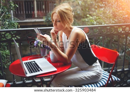 Beautiful women reading news on her cell telephone while relaxing after viewing the film on portable laptop computer, young female using mobile phone after work on net-book during recreation time