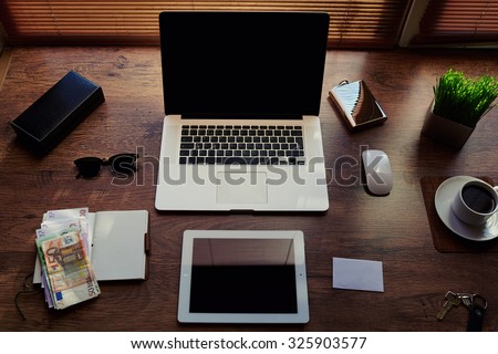 Mock up of successful person desktop with luxury accessories and distance work tools, portable laptop computer, digital tablet with blank copy space screen, money bills, notepad and cup of coffee