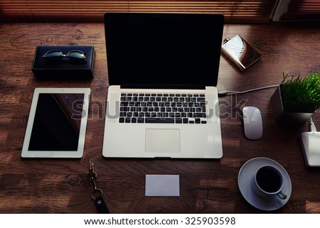 Mock up of office or home desktop with gadgets and work tools, blank screen portable laptop computer, mouse, sunglasses, digital tablet, empty touch pad, white envelope, modern hipster workspace