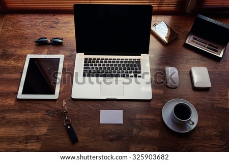 Mock up of modern freelance desktop with accessories and distance work tools, blank screen laptop computer and digital tablet, sunglasses, cup of coffee, touch pad and hard drive, business workspace