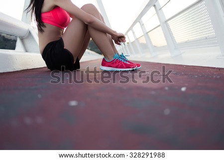 Cropped image of young athletic woman dressed in colorful sportswear relaxing after workout out while sitting on asphalt road with copy space area, athletic female rest after fitness training outside