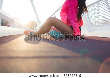 Young female jogger in tracksuit taking break between intense exercising outdoors while sitting on a asphalt road with copy space area , fit women dressed in sport wear relaxing after workout outside