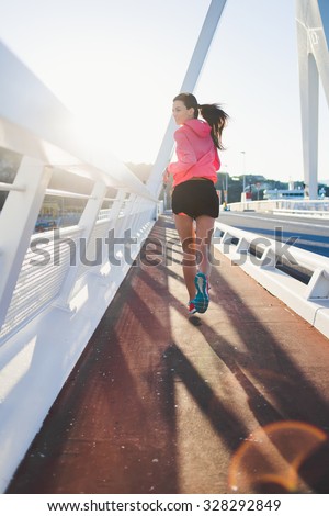 Back view of a young brunette athletic woman with perfect slender figure running on the bridge against sunset, sporty female dressed in sportswear jogging in the fresh air during her recreation time